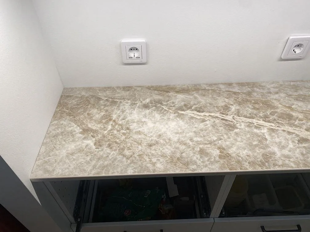 Närbild av polerad Dekton Taga köksbänkskiva med gråbeige ådring och vägguttag i kök i Hindås.