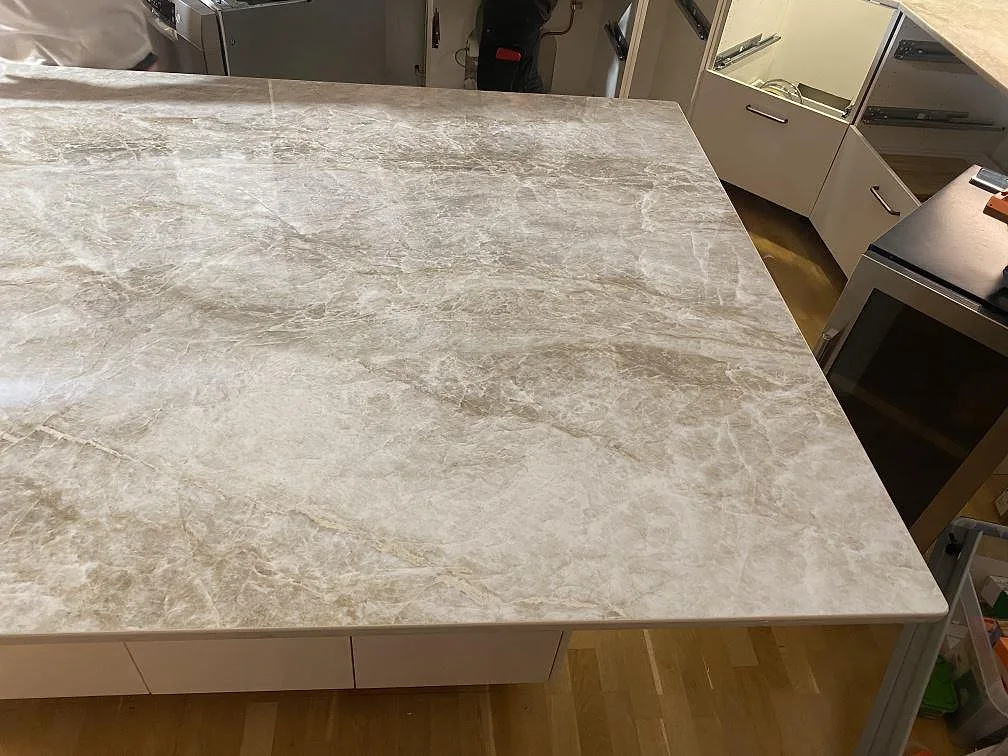 Köksö i polerad Dekton Taga keramik med mjuk beige ådring, fotad ovanifrån under monteringen i ett kök i Hindås.