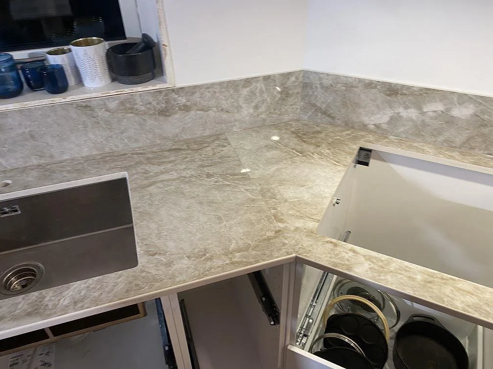 Köksbänkskiva i Dekton Taga med uppvikt stänkkant och underlimmad rostfri diskho i ett hörn av ett kök i Hindås.