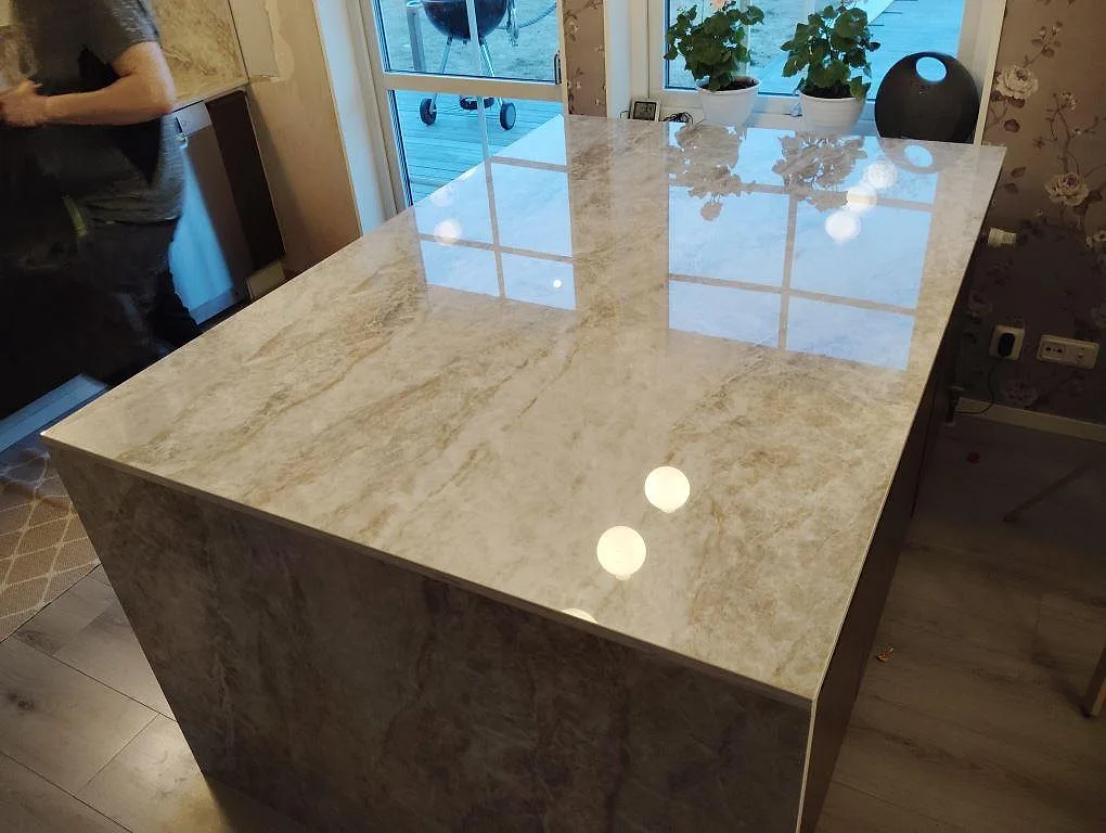 Stor polerad köksö i Dekton Taga med beige och grå ådring, mörk köksinredning och pendellampor i ett kök i Hudiksvall.