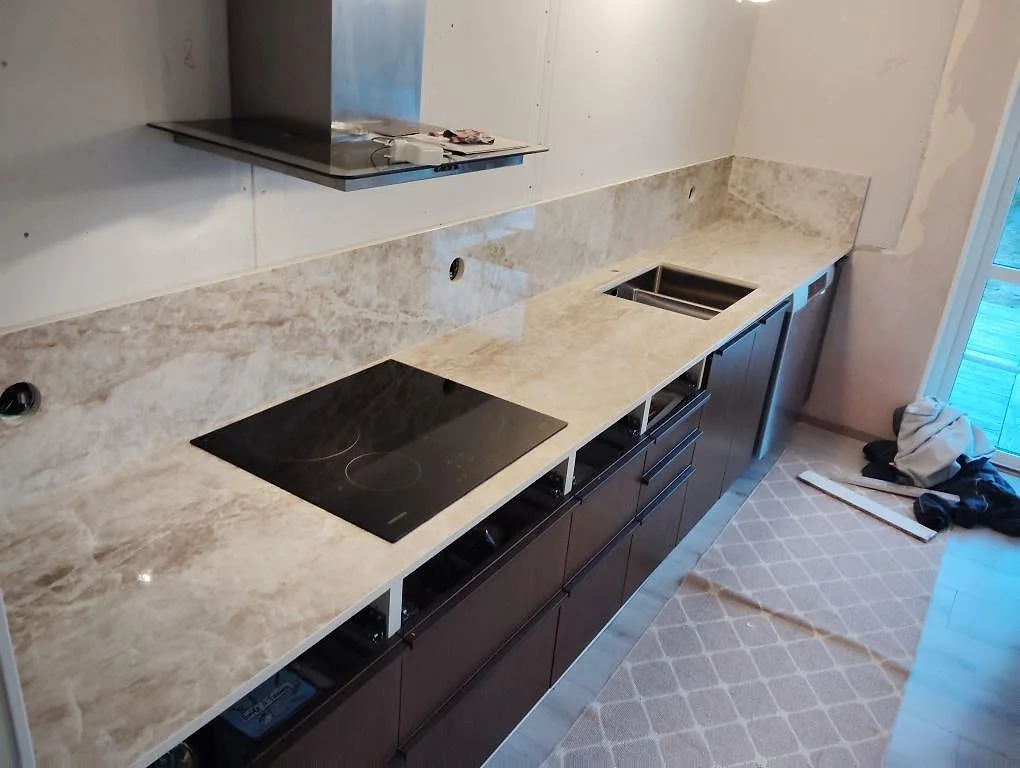 Köksbänkskiva i polerad Dekton Taga med induktionshäll, underlimmad rostfri diskho och stänkskydd längs mörka köksskåp i Hudiksvall.
