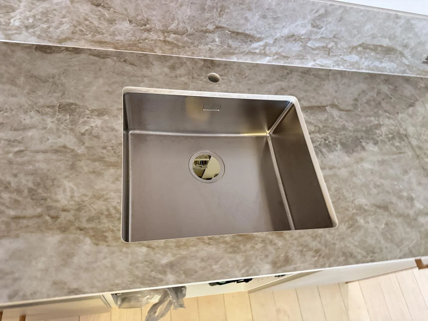 Detalj av rostfri diskho i en polerad köksbänkskiva i Dekton Taga, keramik, med gråbeige ådring i Köpenhamn V.