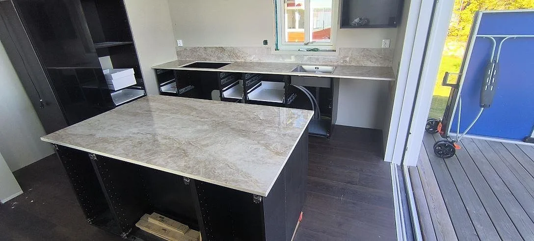 Köksbänkskiva och köksö i polerad Dekton Taga keramik med stänkskydd, diskho och hällurtag i ett kök i Köping.
