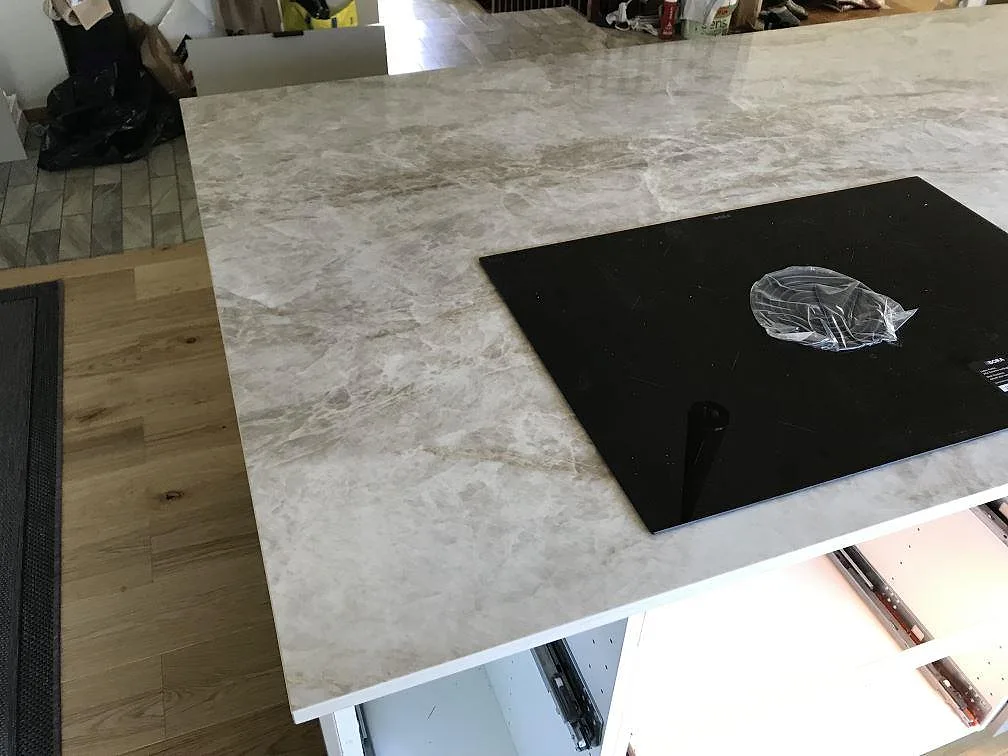Köksbänkskiva i Dekton Taga med varm greige ådring och infälld induktionshäll, sedd i ögonhöjd i ett kök i Limhamn.