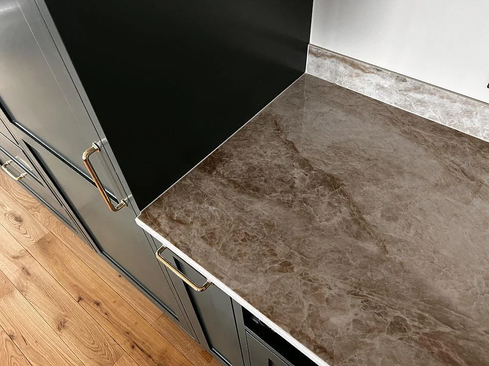 Detalj av polerad Dekton Taga keramik på köksbänk intill mörkgrön inredning och trägolv i Limhamn.