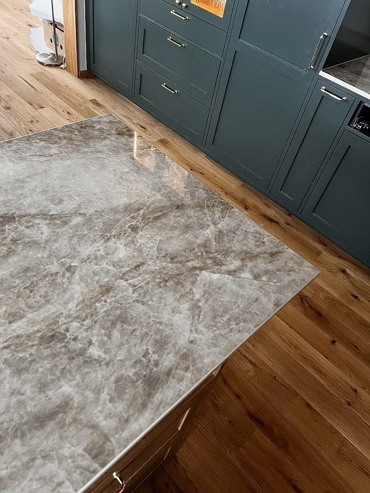 Köksö i polerad Dekton Taga keramik med gråbeige ådring, träinredning och mörkgröna köksskåp i Limhamn.