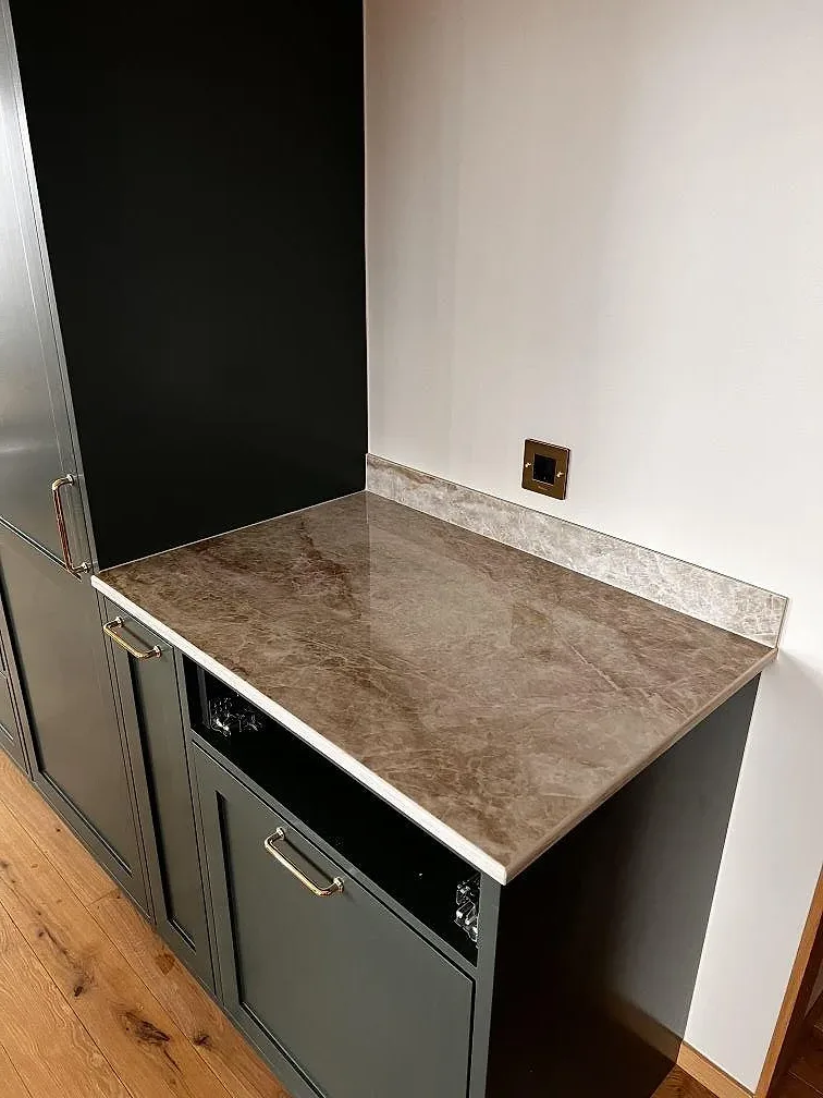 Köksbänkskiva i polerad Dekton Taga keramik med uppvikt stänkkant och mörkgröna luckor i Limhamn.
