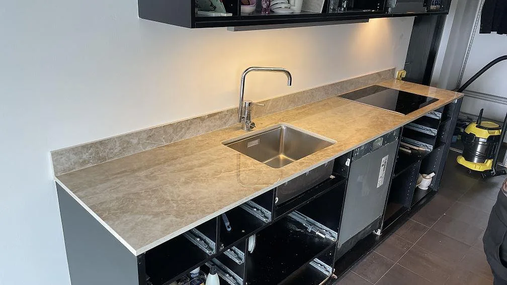 Köksbänkskiva i polerad keramisk Dekton Taga med kort stänkkant, rostfri diskho och häll i ett kök i Malmö.