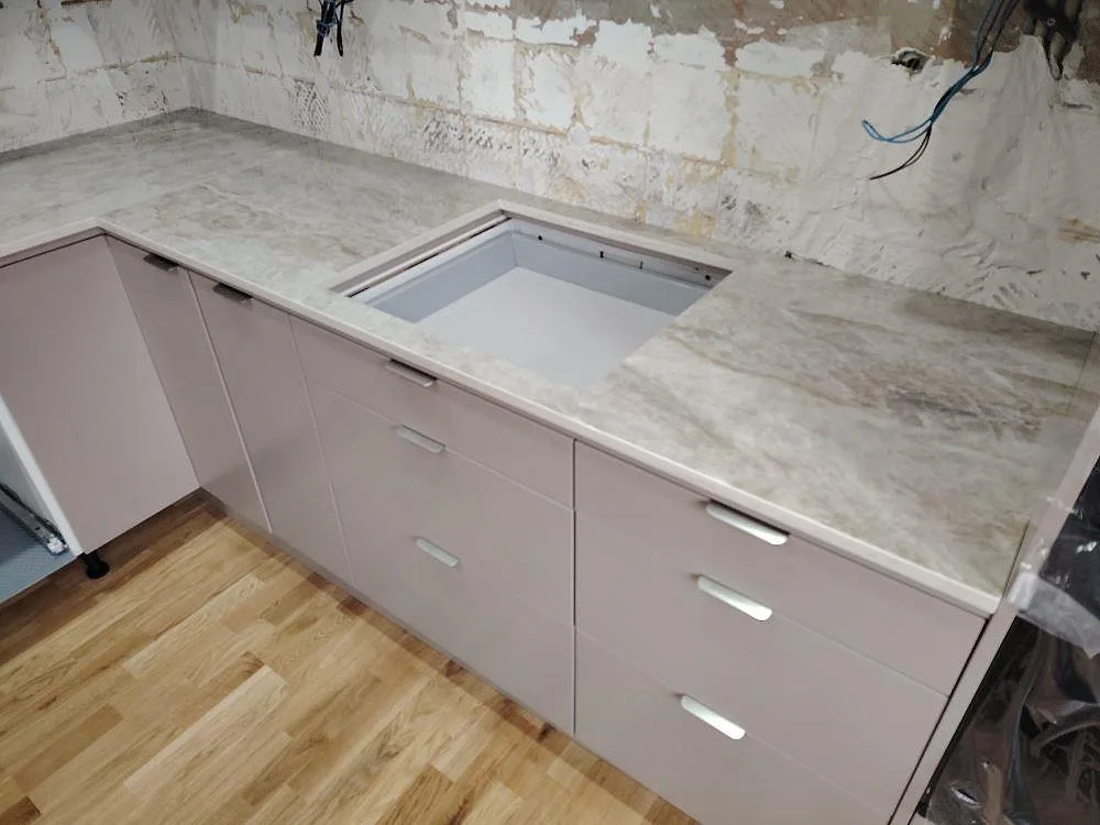 Polerad Dekton Taga bänkskiva i ljus keramik med rektangulärt urtag och synlig ådring på skåpsrad i Norsborg.