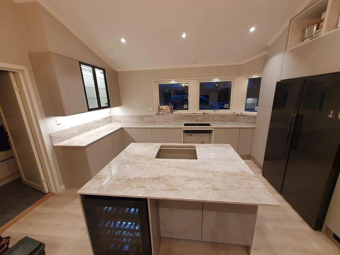 Köksbänkskiva och köksö i polerad Dekton Taga keramik med varm, marmorlik ådring och infälld induktionshäll i ett U-format kök i Sigtuna.