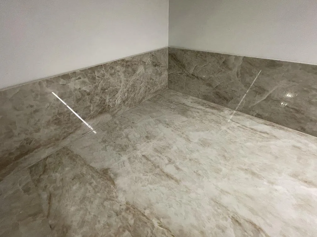 Närbild på polerad Dekton Taga där bänkskiva och uppvikt stänkskydd möts i en hörna, varmgrå betongliknande keramik i ett kök i Stockholm.