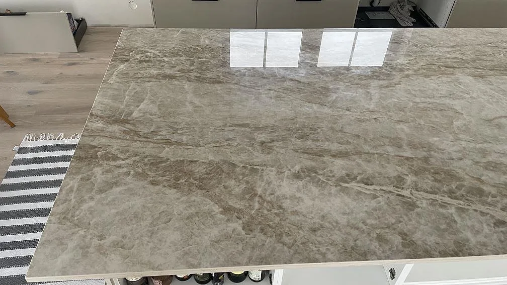 Närbild på polerad Dekton Taga köksö med blank yta, gråbeige ådring och ljusreflexer i Trelleborg.