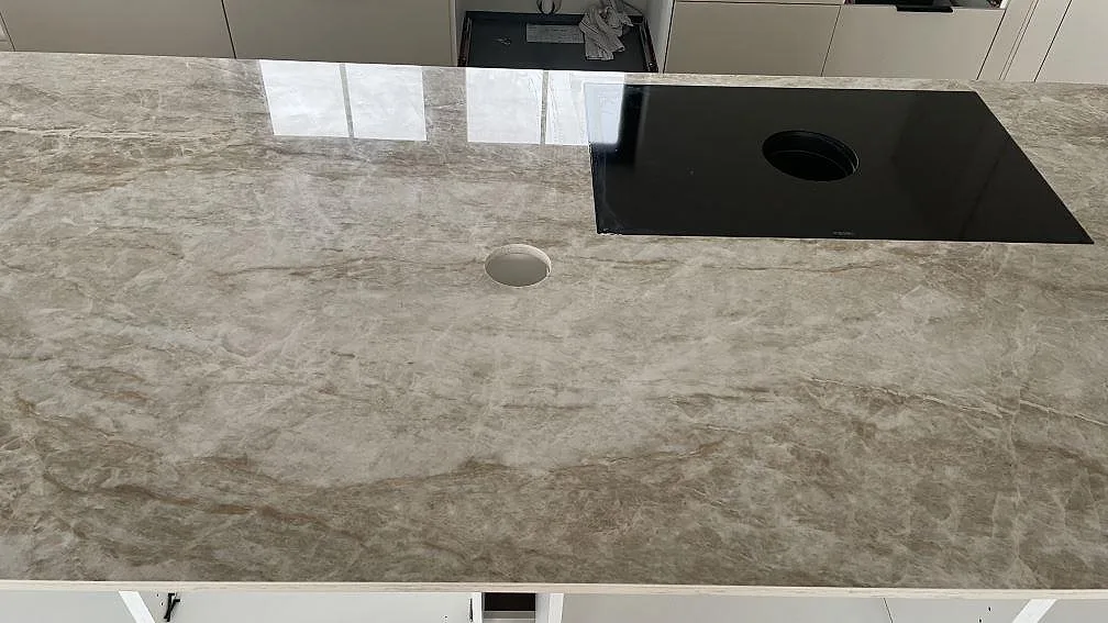 Köksö i polerad Dekton Taga med svart häll och rund utskärning i ett kök under montering i Trelleborg.