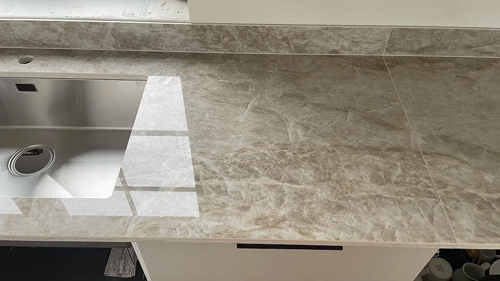 Väggbänk i polerad Dekton Taga med låg stänkkant och gråbeige ådring under fönster i Trelleborg.