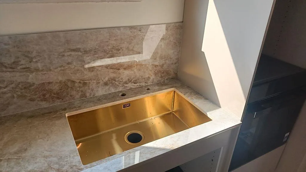Diskbänksdel i polerad Dekton Taga, keramik, med stänkskydd och diskho vid fönster i Trollhättan.