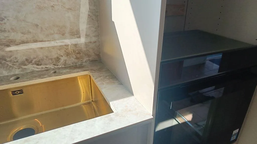 Detalj av köksbänkskiva i polerad Dekton Taga vid diskho och högskåp under montering i Trollhättan.