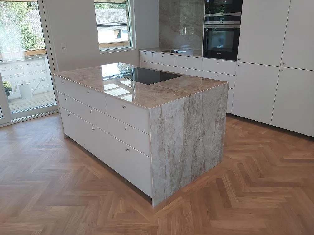 Köksö med vattenfallsklädda sidor i polerad Dekton Taga, vit köksinredning och fiskbensparkett i TYresö.