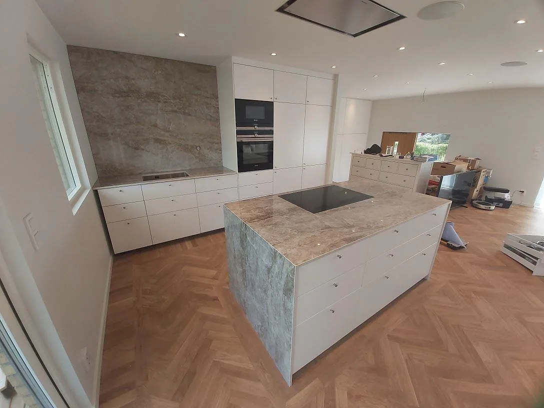 Polerad Dekton Taga som köksbänkskiva och hel väggbeklädnad i ett ljust kök med vit inredning i TYresö.