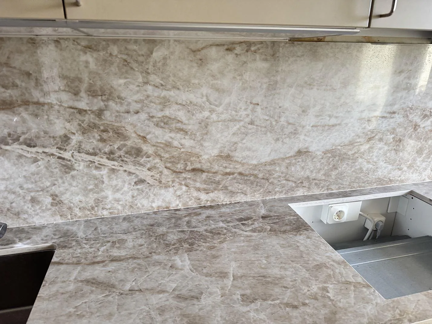 Polerad köksbänkskiva i Dekton Taga med hällurtag och hög stänkyta i samma gråbeige keramik i ett kök i Västra Frölunda.