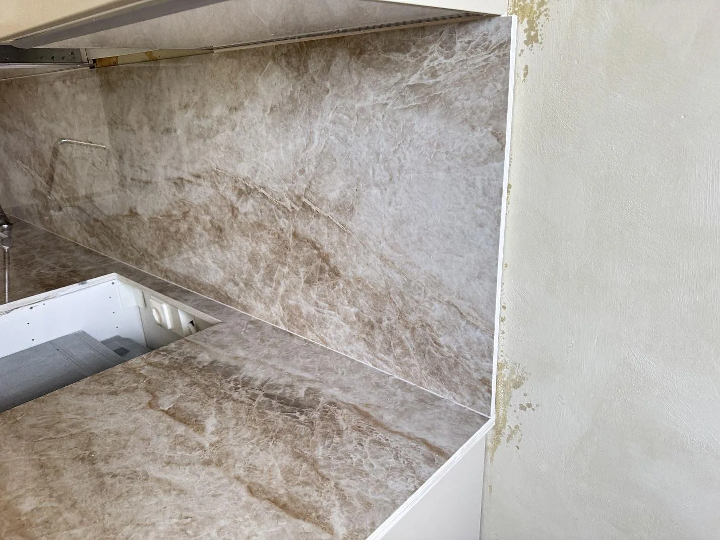 Vinklad detalj av köksbänkskiva och väggbeklädnad i polerad Dekton Taga keramik vid hällurtaget i Västra Frölunda.
