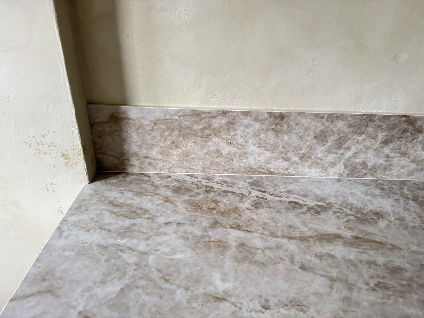 Detalj av polerad Dekton Taga köksbänkskiva med uppvikt stänkkant och gråbeige ådring vid vägg i Västra Frölunda.