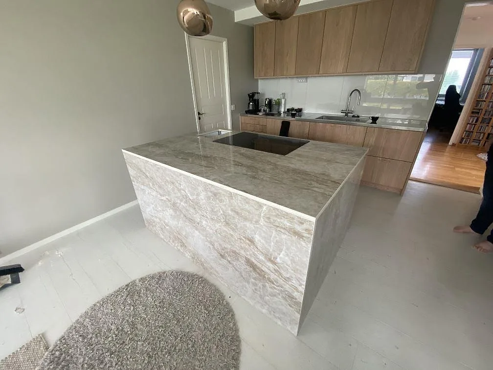 Köksbänkskiva och köksö i Dekton Taga, polerad greige keramik med infälld induktionshäll, i ett ljust kök i Växjö.