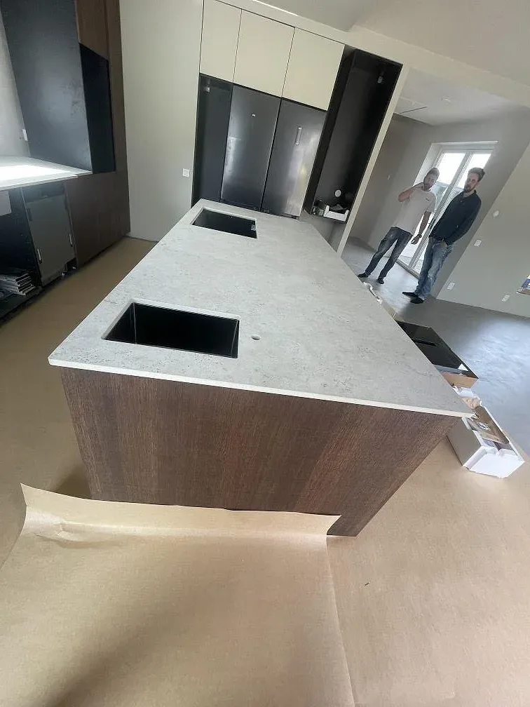 Frihängande köksö i matt Dekton Tk05 Sabbia med diskho- och hällurtag i ett kök under montering i Alingsås.