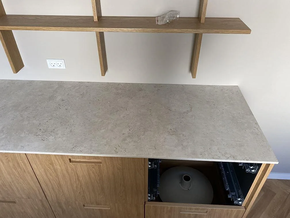 Köksbänkskiva i matt Dekton Tk05 Sabbia över träskåp med öppen stomme under montering i Birkerød.