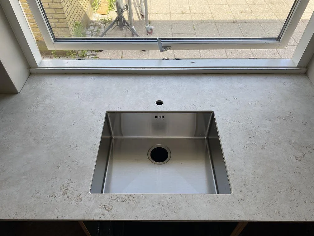 Underlimmad rostfri diskho i en matt köksbänkskiva av Dekton Tk05 Sabbia vid fönster i Birkerød.