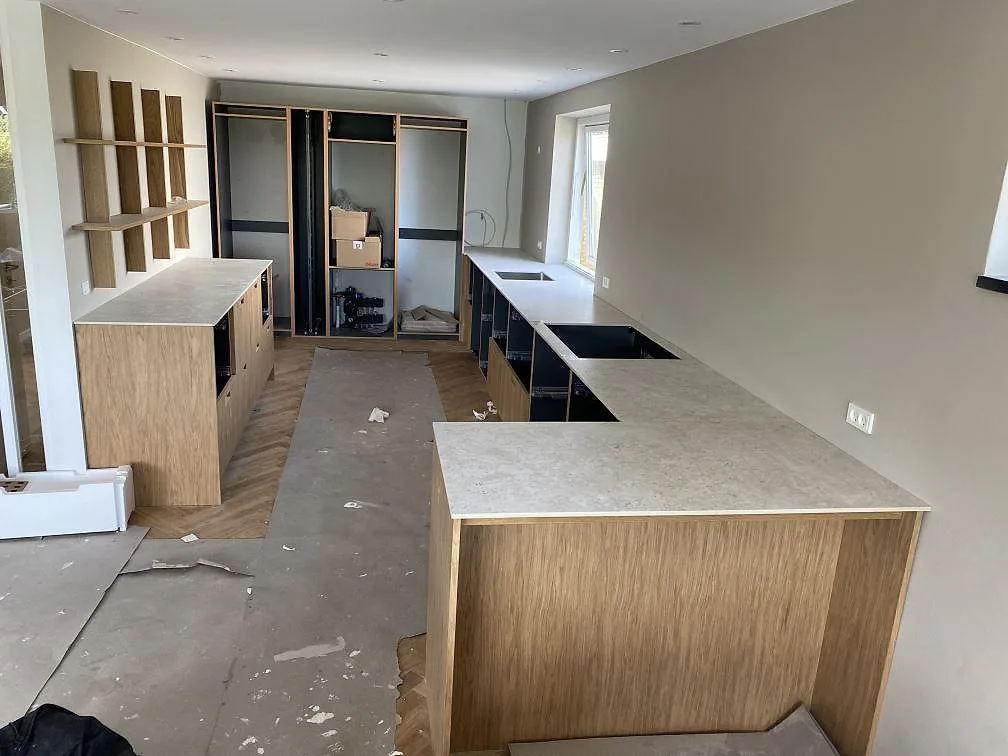 Köksbänkskiva i matt Dekton Tk05 Sabbia med ljus stenyta på köksstommar i trä under montering i Birkerød.