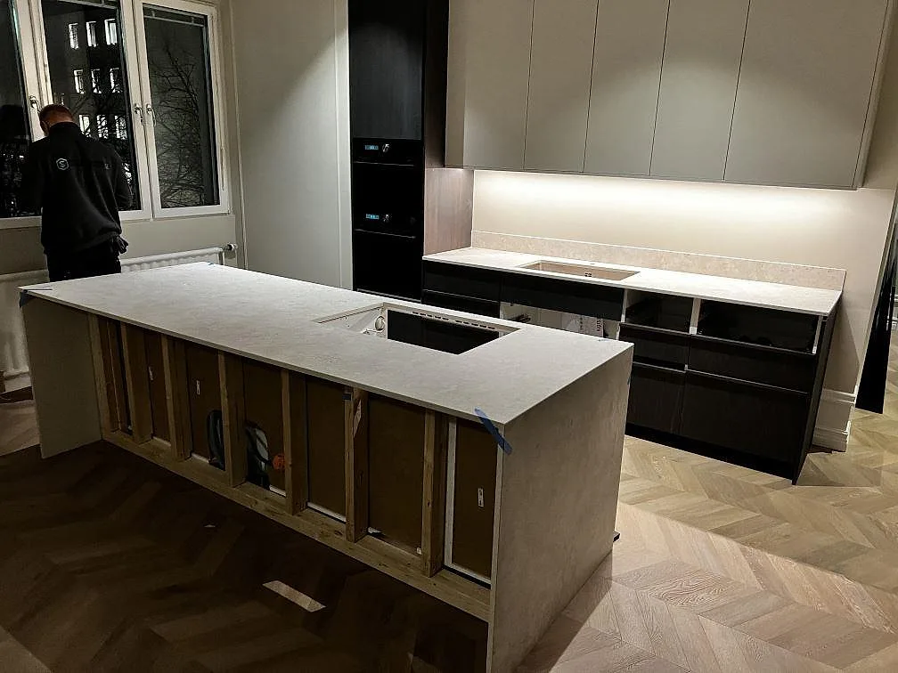 Köksbänkskiva och köksö i matt Dekton Tk05 Sabbia med hälluttag, stänkskydd och mörka köksstommar i Göteborg.