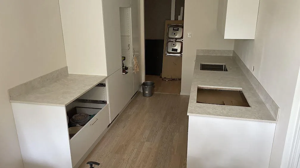 Matt köksbänkskiva i Dekton Tk05 Sabbia med stänkskydd, diskho och hällöppning i ett kök under montering i Halmstad.