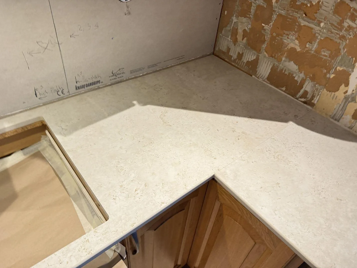 Bänkskiva i Dekton TK05 Sabbia i L-format kök i Hasslö med kalkstensliknande yta mot exponerad tegelvägg, fotat under montering.