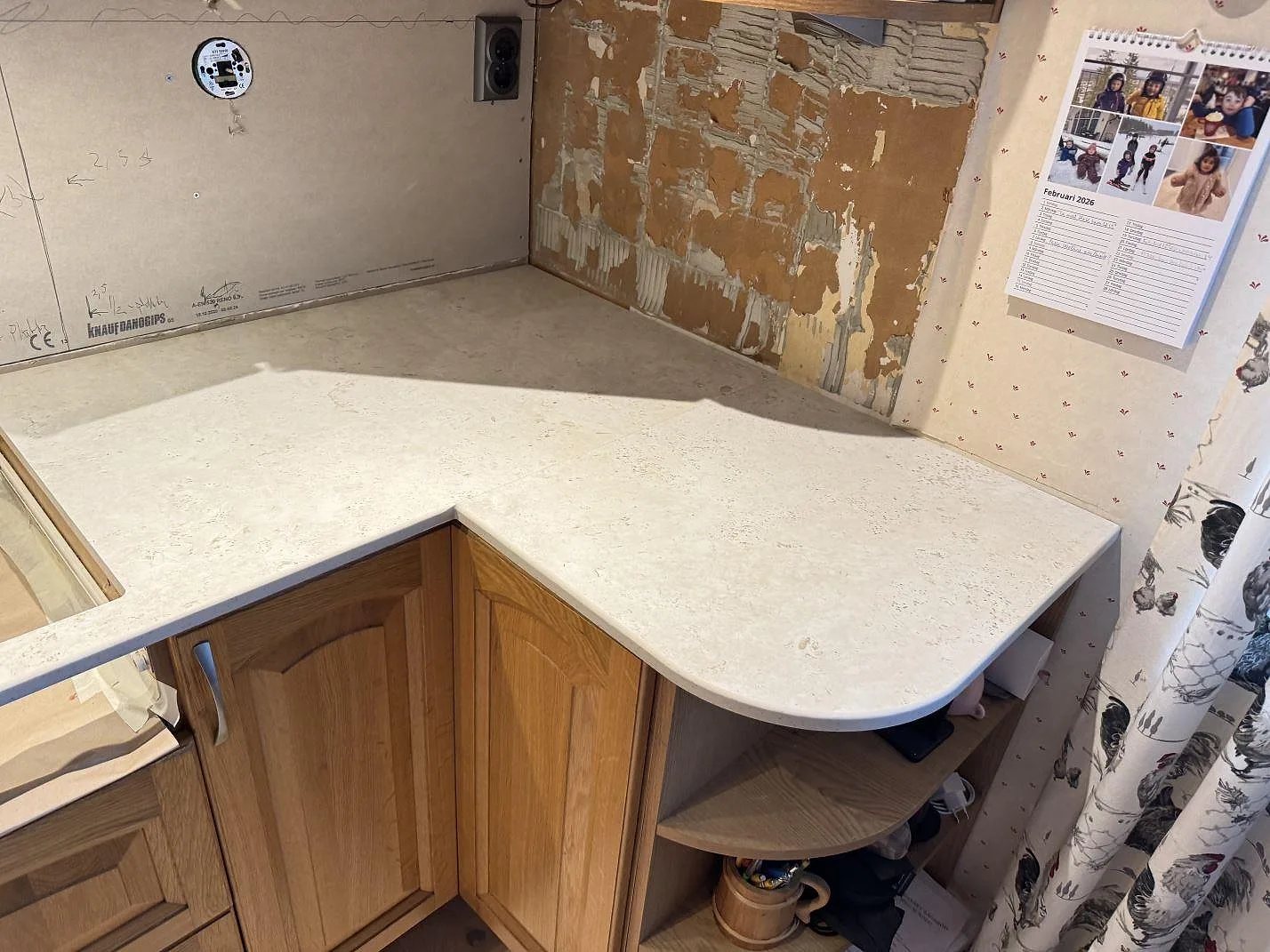 Köksbänkskiva i matt Dekton TK05 Sabbia med rundad halvö och ekstommar i ett kök i Hasslö, tagen under montering mot bar gipsvägg.