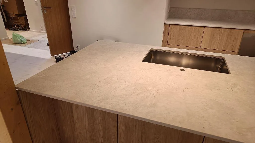 Närbild på matt Dekton Tk05 Sabbia i köksö med rostfri diskho och beige stenstruktur i ett kök i Höllviken.