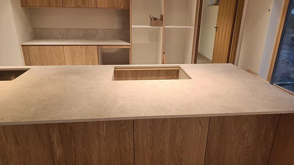 Matt bänkskiva i Dekton Tk05 Sabbia med öppning för häll och låg stänkkant vid väggbänken i Höllviken.