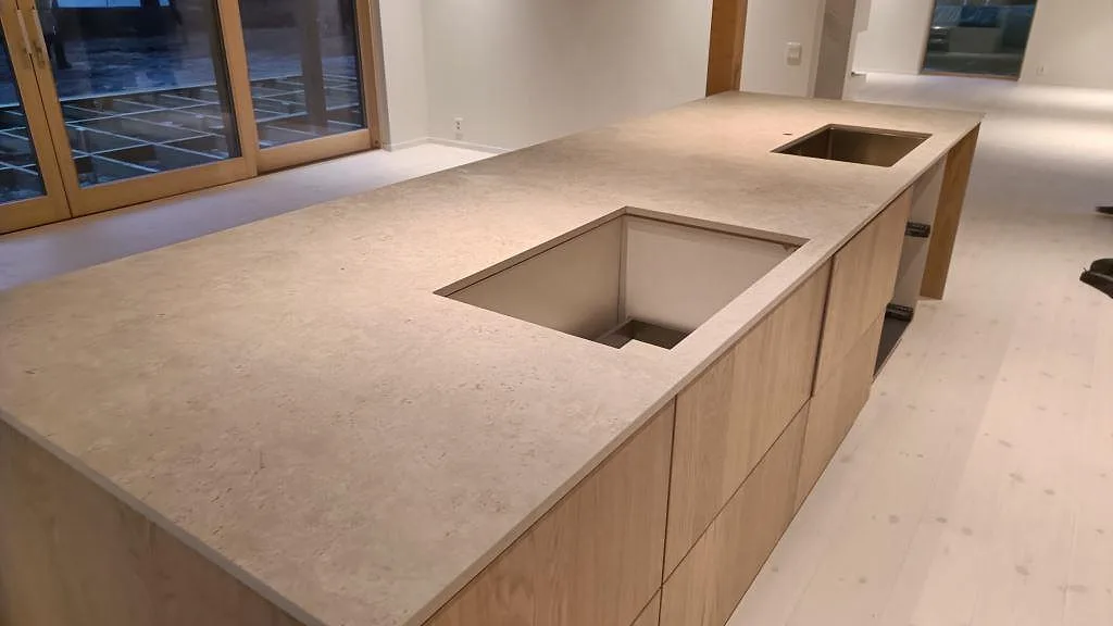 Köksö i matt Dekton Tk05 Sabbia med synliga urtag för häll och rostfri diskho, beige keramisk bänkskiva i Höllviken.