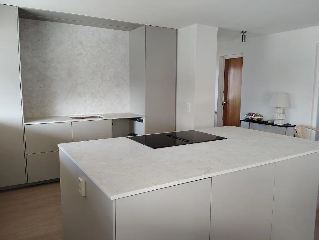 Köksbänkskiva i matt Dekton Tk05 Sabbia med häll i köksö och väggbeklädnad i ett kök i Köping.