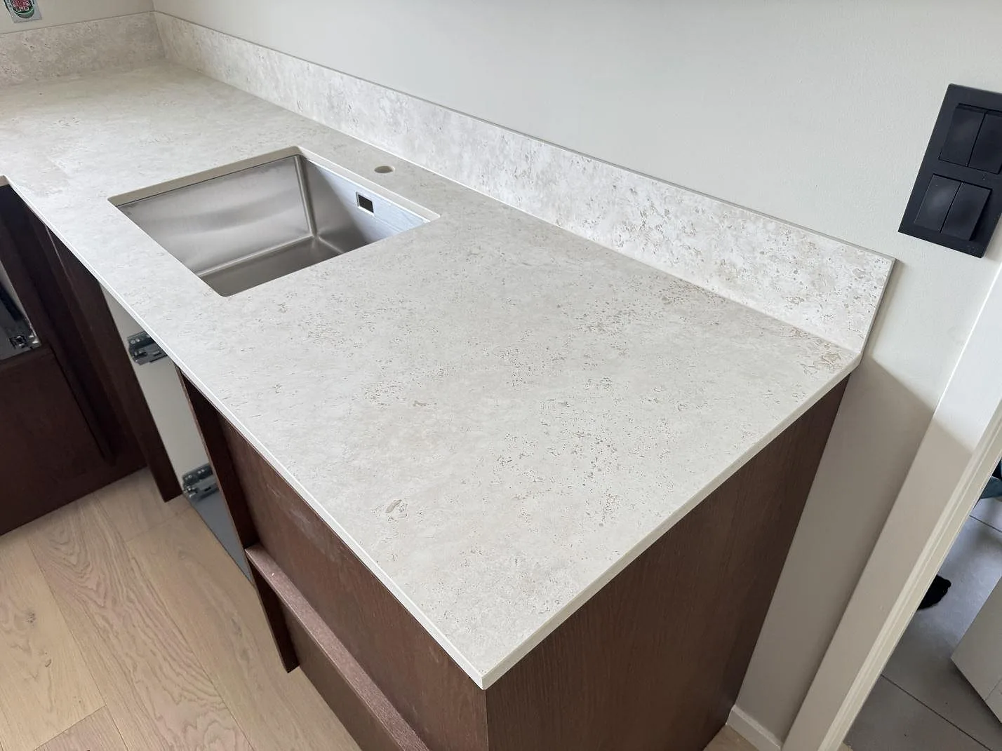 Vinkelbild av matt Dekton Tk05 Sabbia med rostfri diskho, stänkskydd och mörka trästommar i Lindome.
