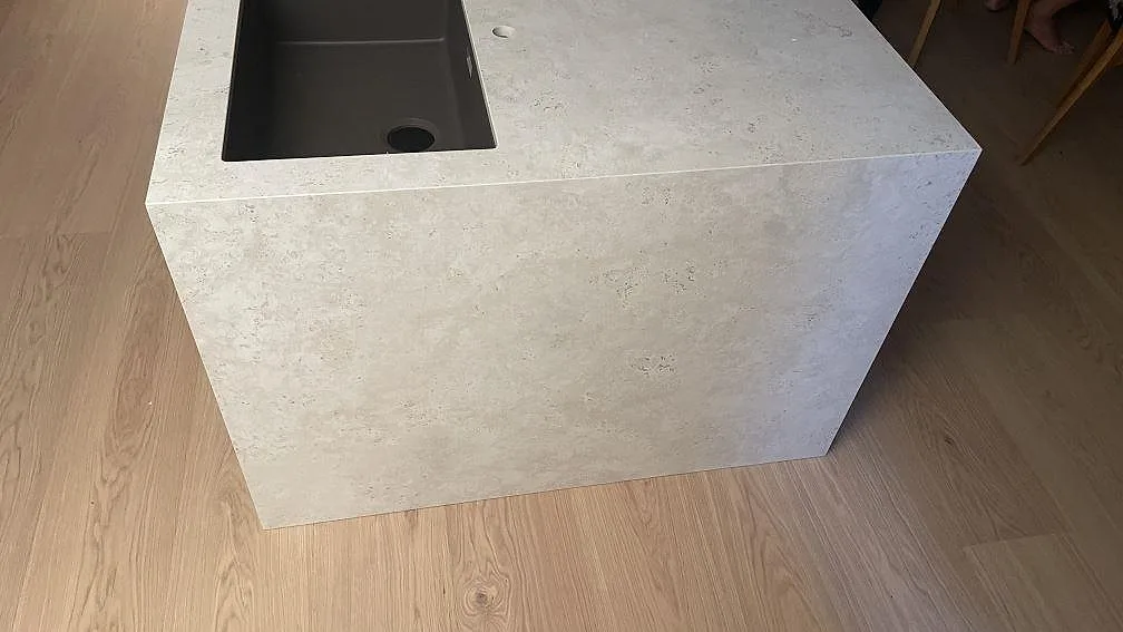 Köksö i matt Dekton Tk05 Sabbia med diskho och vattenfallsida mot trägolv i Lomma.
