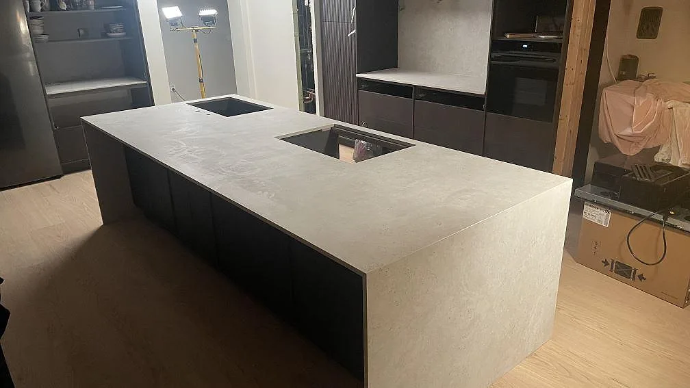 Köksö och bänkskiva i matt Dekton Tk05 Sabbia med vattenfallsida, diskho och hälluttag i ett kök i Lomma.