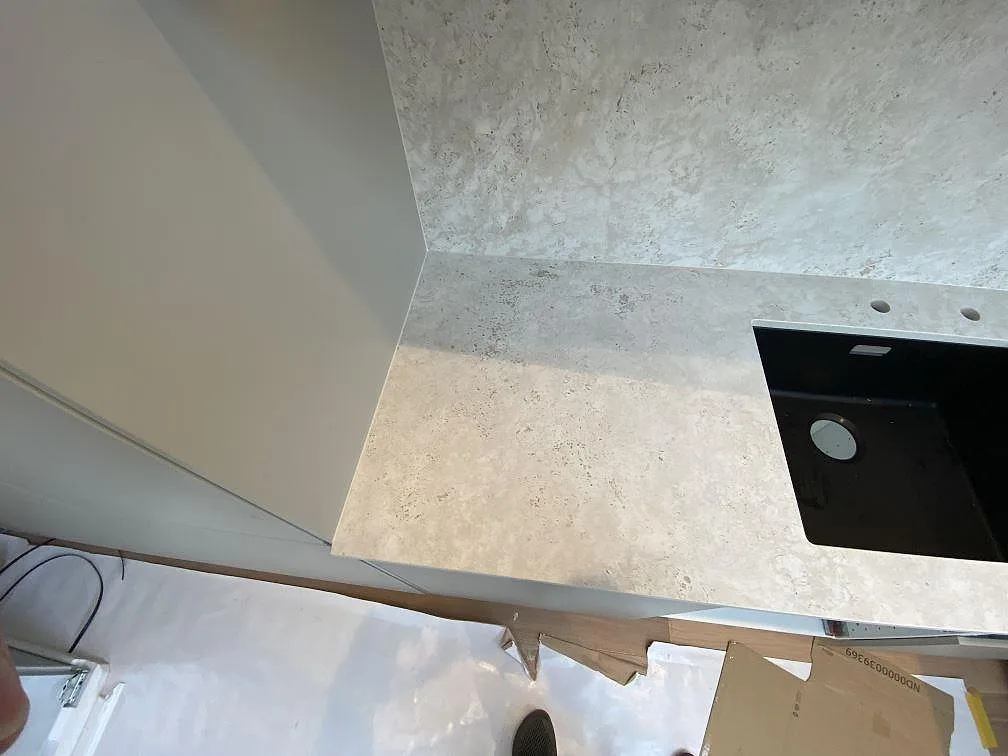 Närbild av matt Dekton Tk05 Sabbia som köksbänk och stänkskydd intill högskåp och mörk diskho i Malmö.