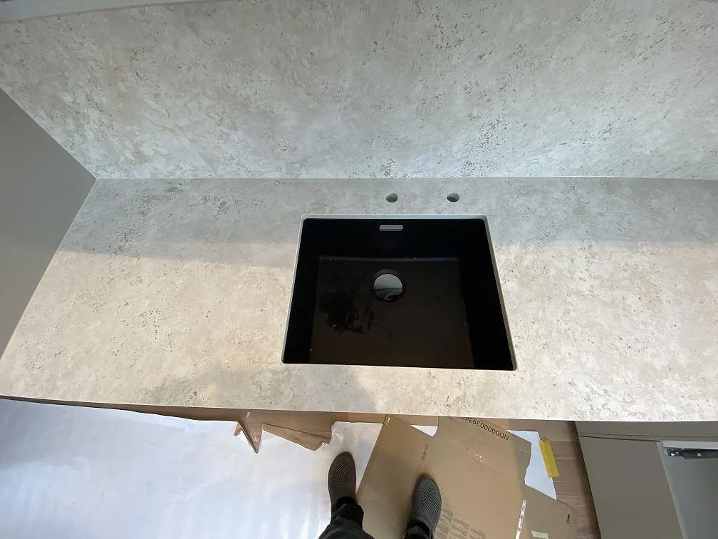 Svart diskho i köksbänkskiva av matt Dekton Tk05 Sabbia med matchande stänkskydd och blandarhål i Malmö.