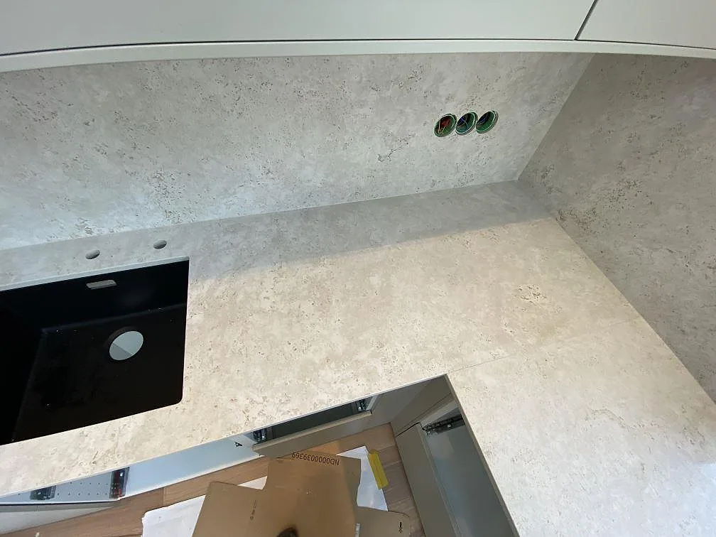 Detalj av matt Dekton Tk05 Sabbia runt diskhozon, med stänkskydd och synliga eluttag i kök i Malmö.