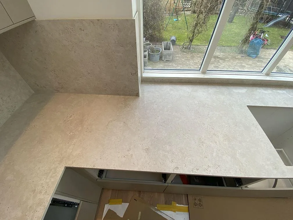 Ljus köksbänkskiva i matt Dekton Tk05 Sabbia längs fönstervägg med 8 mm stänkskydd i Malmö.