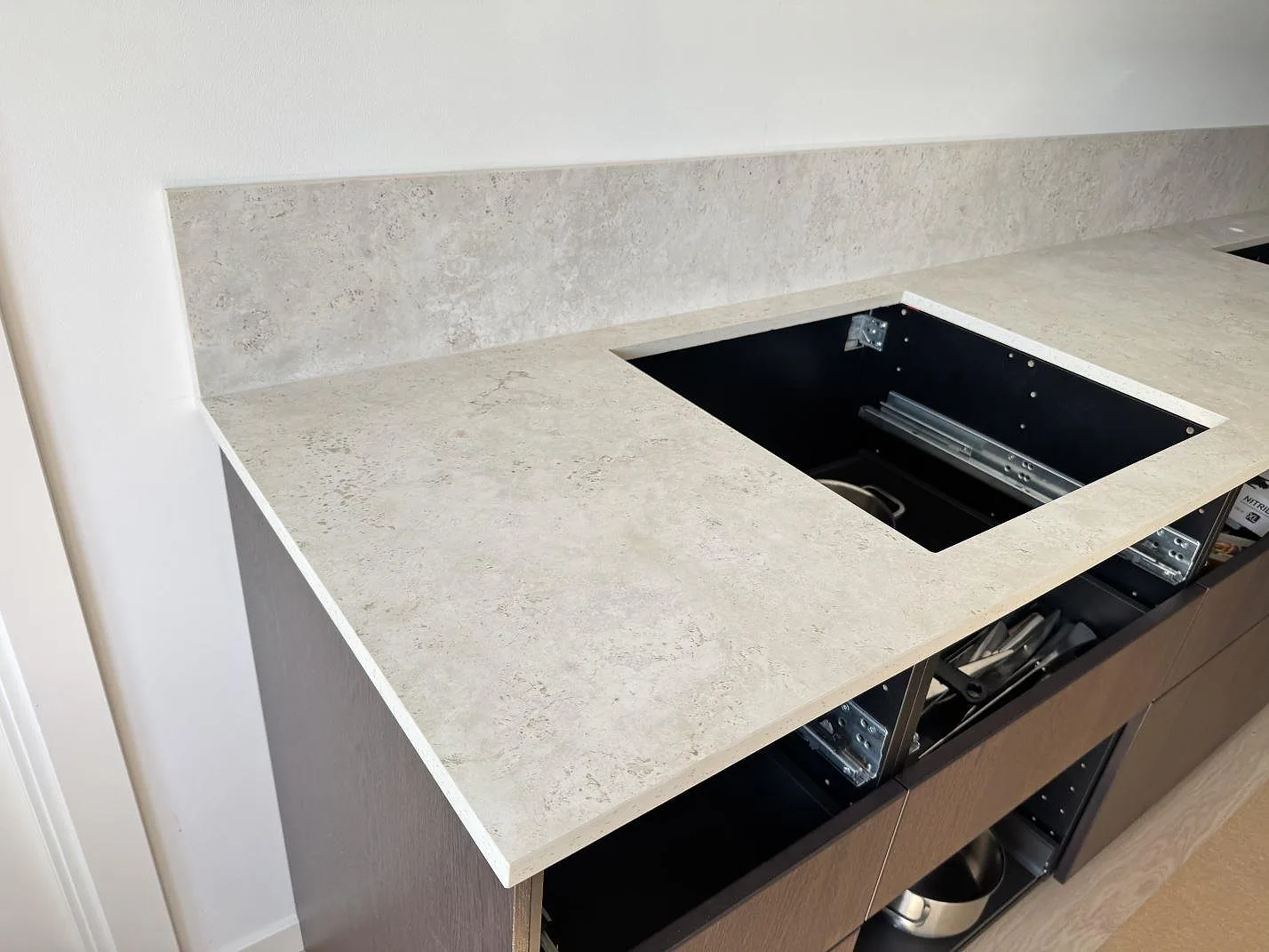 Köksbänkskiva i matt Dekton Tk05 Sabbia med hällurtag, stänkskydd och öppna köksstommar under montering i Malmö.