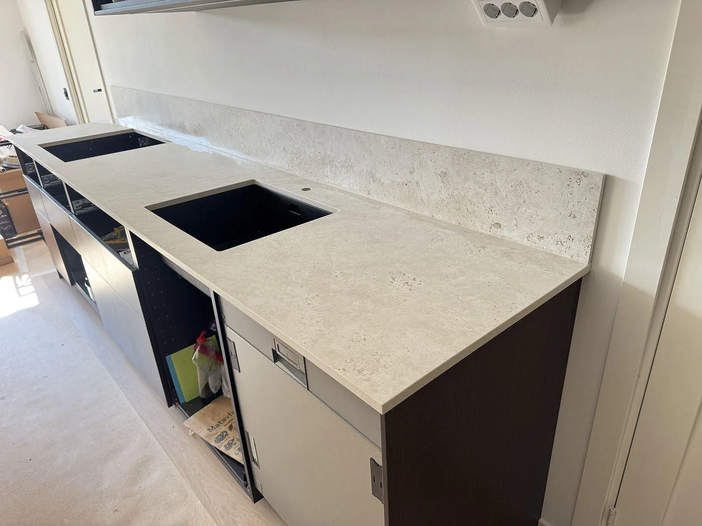 Lång köksbänkskiva i matt Dekton Tk05 Sabbia, keramik, med stänkskydd och två urtag i ett kök under montering i Malmö.