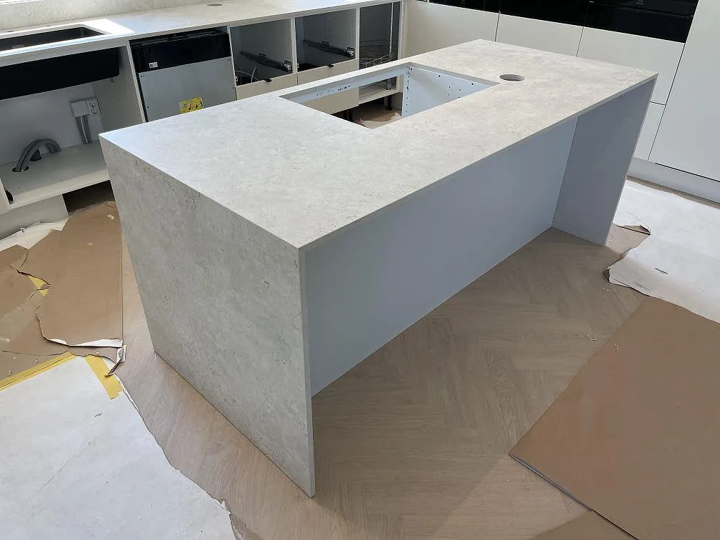 Köksö i matt Dekton Tk05 Sabbia med större hällurtag, rund öppning och vattenfallssida i ett kök under montering i Örebro.