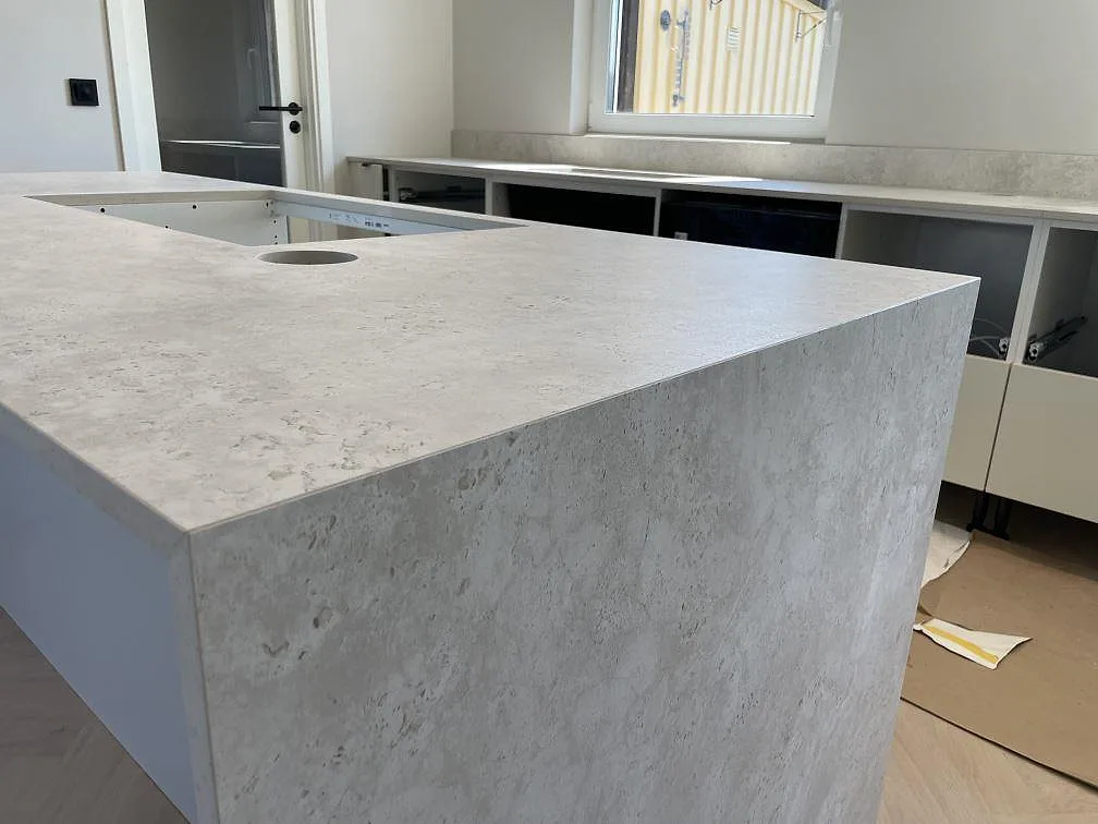 Detalj av köksö i matt Dekton Tk05 Sabbia med sandbeige struktur, tunn kant och bänkskiva längs fönstervägg i Örebro.