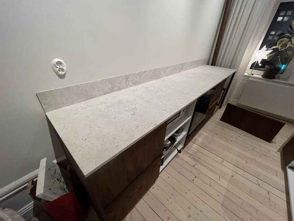 Rak väggbänk i matt Dekton TK05 Sabbia med lågt stänkskydd och mörka trästommar i ett kök i Stockholm.